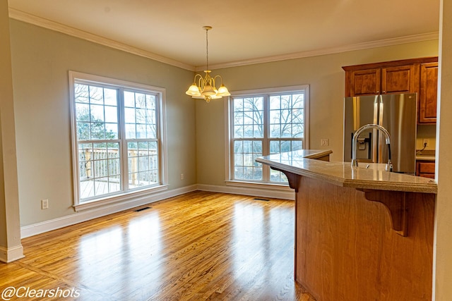 kitchen with stainless steel refrigerator with ice dispenser, a kitchen bar, crown molding, a chandelier, and pendant lighting