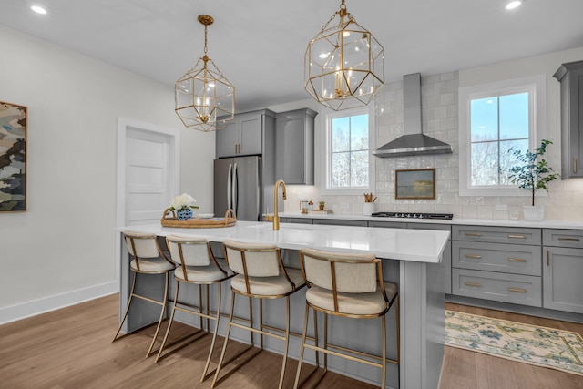 kitchen featuring stainless steel appliances, wall chimney exhaust hood, gray cabinetry, and an island with sink