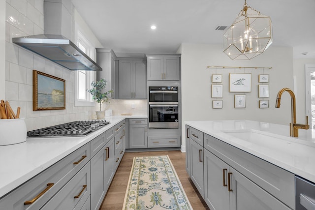 kitchen featuring wall chimney exhaust hood, sink, backsplash, gray cabinetry, and stainless steel appliances