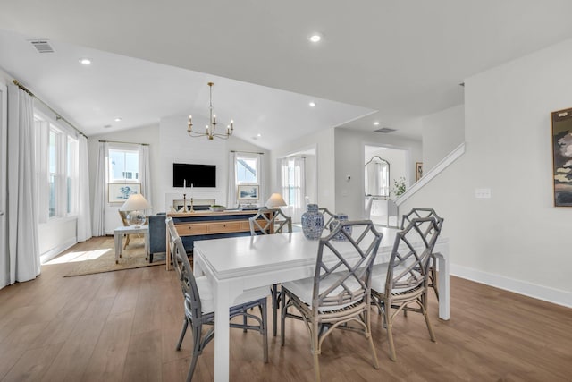 dining space with hardwood / wood-style flooring, vaulted ceiling, a healthy amount of sunlight, and an inviting chandelier