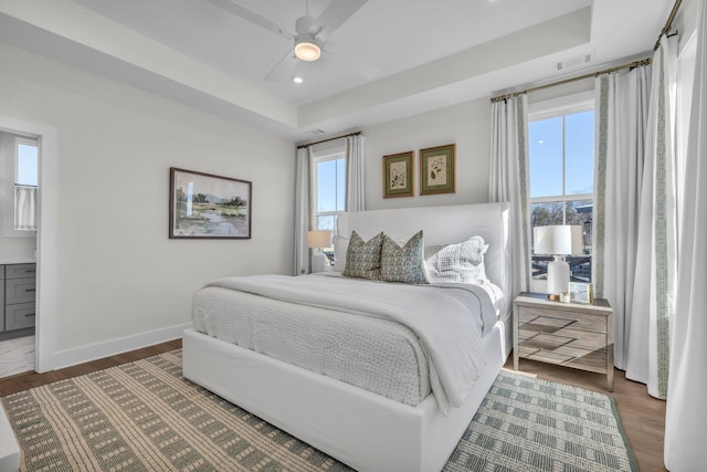 bedroom with ceiling fan, ensuite bathroom, a raised ceiling, and dark hardwood / wood-style floors