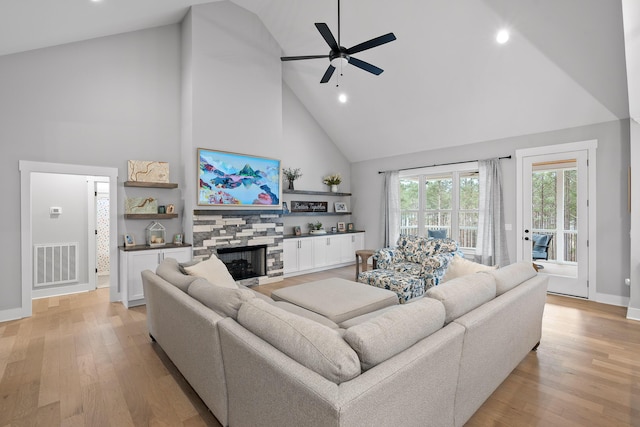 living room with high vaulted ceiling, ceiling fan, a stone fireplace, and light wood-type flooring