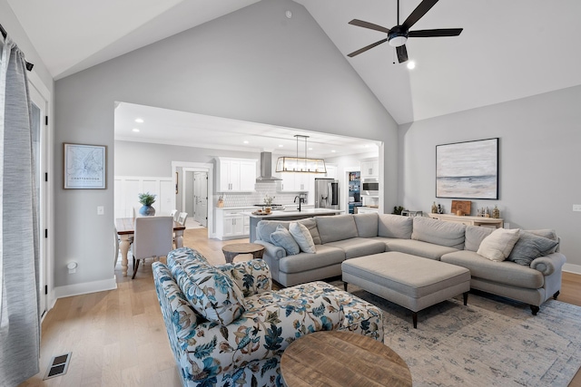 living room with high vaulted ceiling, ceiling fan, and light wood-type flooring