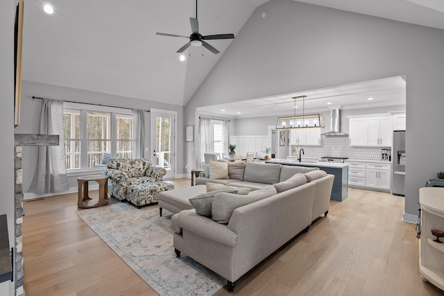 living room featuring sink, ceiling fan with notable chandelier, light hardwood / wood-style flooring, and high vaulted ceiling