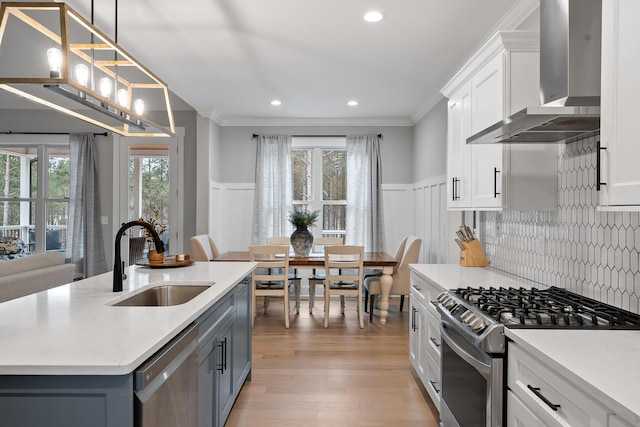 kitchen featuring hanging light fixtures, sink, white cabinetry, wall chimney range hood, and stainless steel appliances