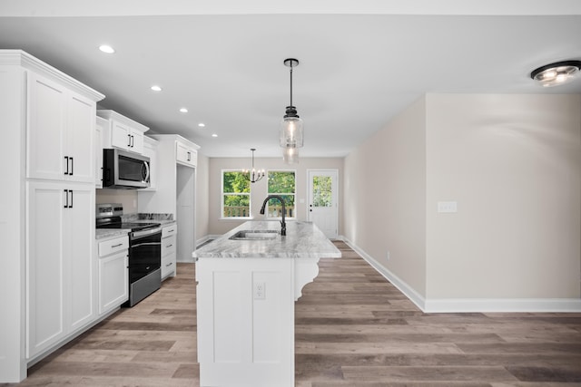 kitchen with sink, decorative light fixtures, white cabinets, stainless steel appliances, and a center island with sink