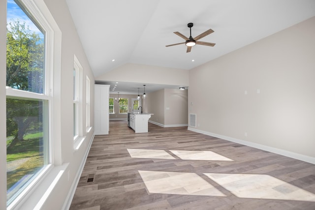 unfurnished living room with ceiling fan with notable chandelier, sink, lofted ceiling, and light wood-type flooring