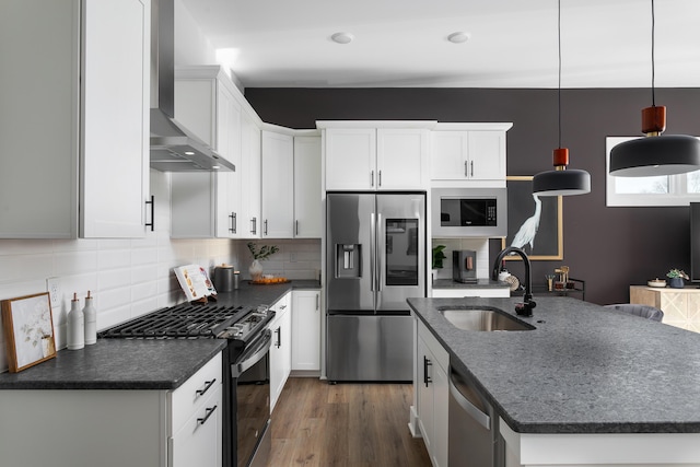 kitchen with pendant lighting, appliances with stainless steel finishes, sink, white cabinets, and wall chimney range hood