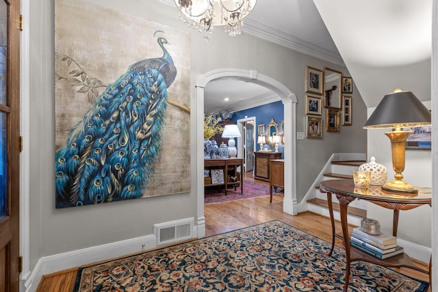 entryway with hardwood / wood-style flooring, crown molding, and a notable chandelier