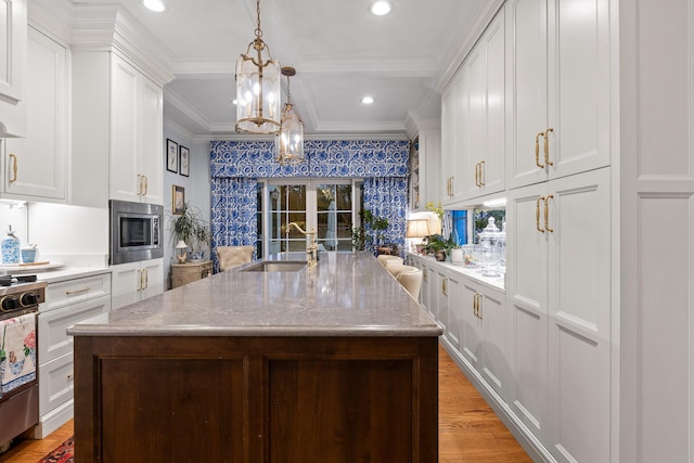 kitchen featuring stainless steel microwave, sink, light wood-type flooring, white cabinets, and a kitchen island with sink