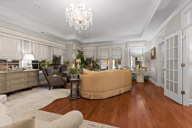 living room with ornamental molding, a chandelier, hardwood / wood-style floors, and a tray ceiling