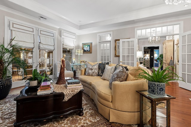 living room with crown molding, hardwood / wood-style floors, an inviting chandelier, and french doors