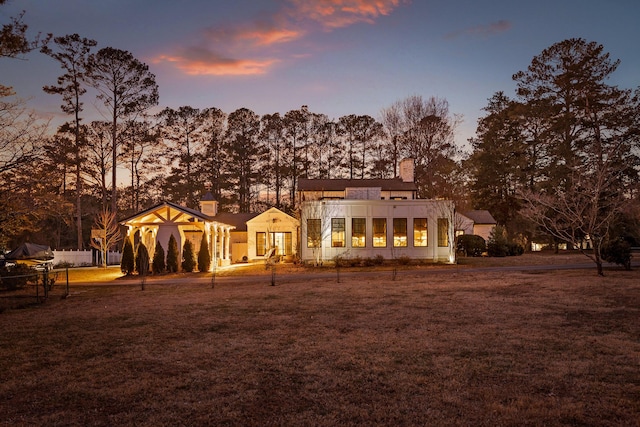 back house at dusk featuring a lawn