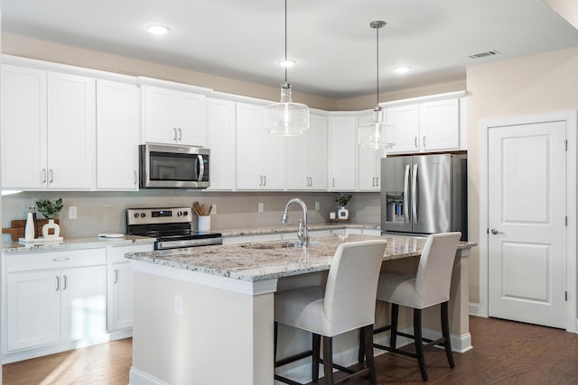 kitchen with appliances with stainless steel finishes, white cabinets, sink, dark hardwood / wood-style flooring, and an island with sink