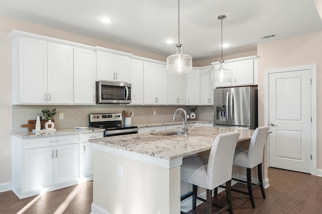 kitchen with pendant lighting, appliances with stainless steel finishes, white cabinetry, sink, and a center island with sink