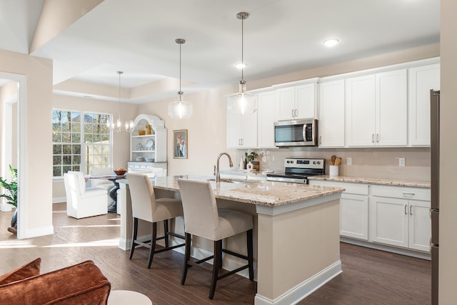 kitchen with pendant lighting, appliances with stainless steel finishes, white cabinetry, an island with sink, and sink