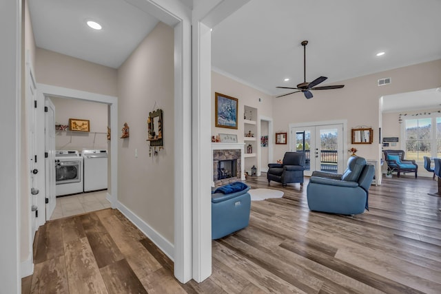 living room with french doors, separate washer and dryer, built in features, a fireplace, and light hardwood / wood-style floors