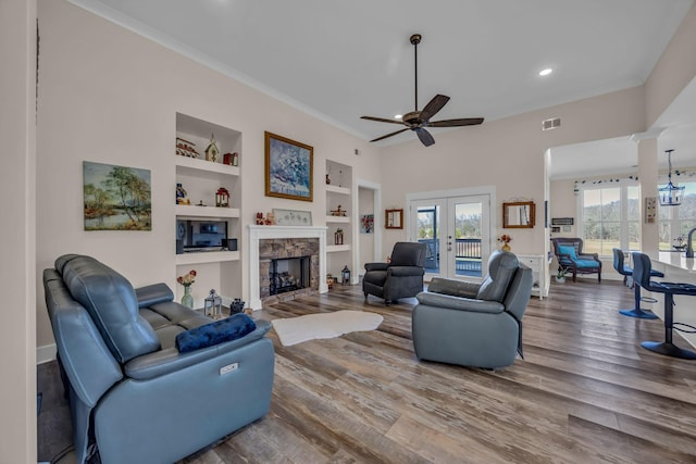 living room with built in shelves, french doors, a stone fireplace, ornate columns, and hardwood / wood-style floors