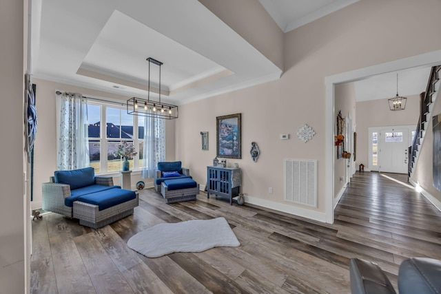 living area featuring crown molding, wood-type flooring, a tray ceiling, and a notable chandelier