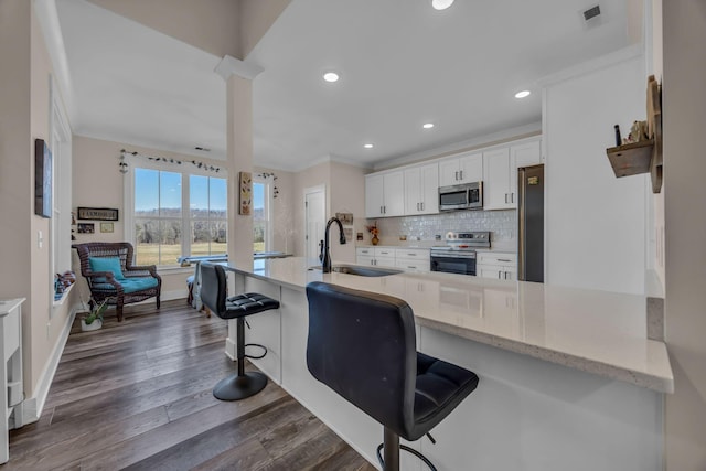 kitchen featuring white cabinetry, appliances with stainless steel finishes, a kitchen bar, and kitchen peninsula