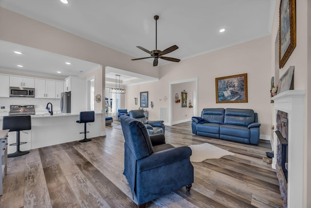 living room featuring ceiling fan with notable chandelier, hardwood / wood-style floors, and a fireplace