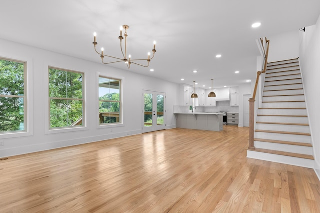 unfurnished living room with a notable chandelier, light wood-type flooring, and french doors