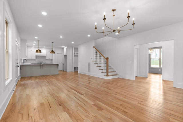 unfurnished living room featuring an inviting chandelier, sink, and light hardwood / wood-style flooring