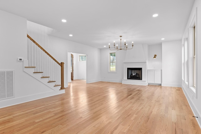 unfurnished living room with an inviting chandelier, a fireplace, and light wood-type flooring