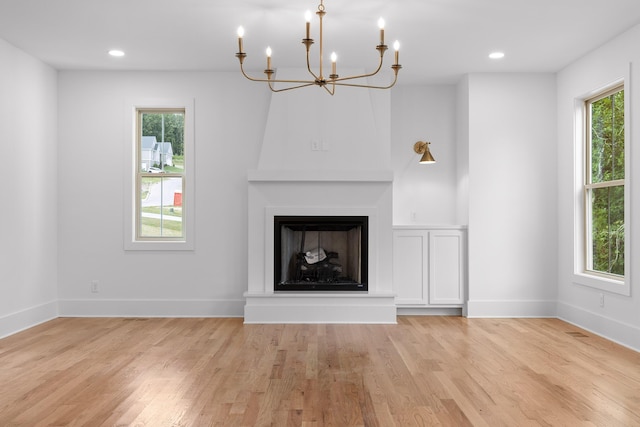 unfurnished living room with a chandelier, a large fireplace, a wealth of natural light, and light wood-type flooring