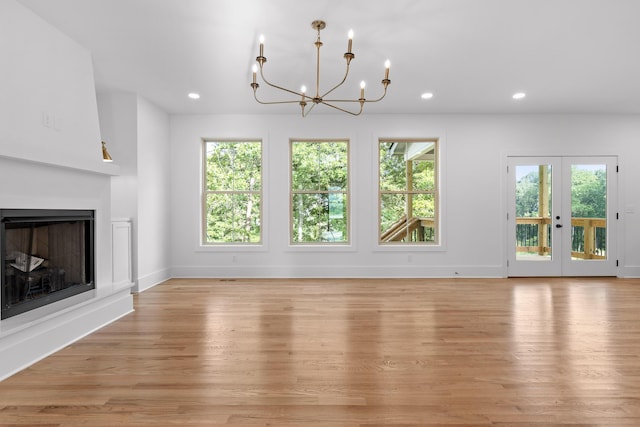 unfurnished living room featuring french doors, a chandelier, and light hardwood / wood-style floors