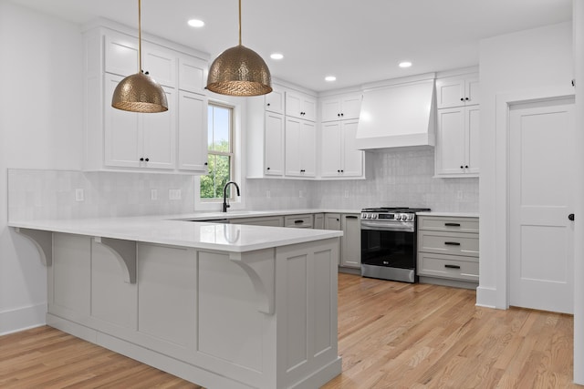 kitchen with wall chimney range hood, hanging light fixtures, stainless steel gas range oven, a kitchen bar, and kitchen peninsula