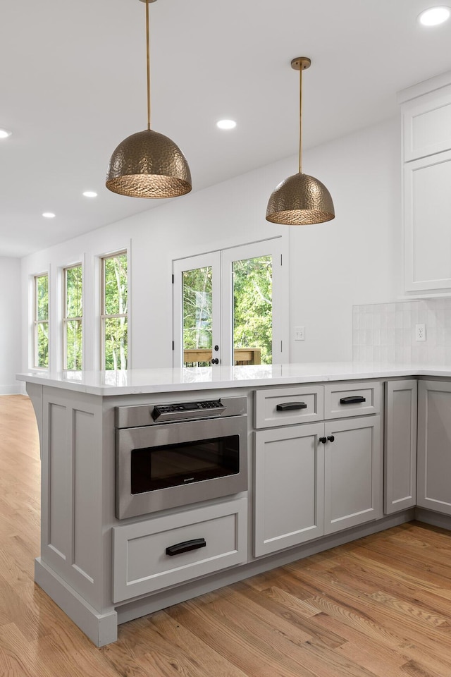 bar featuring gray cabinets, stainless steel microwave, decorative backsplash, decorative light fixtures, and light wood-type flooring