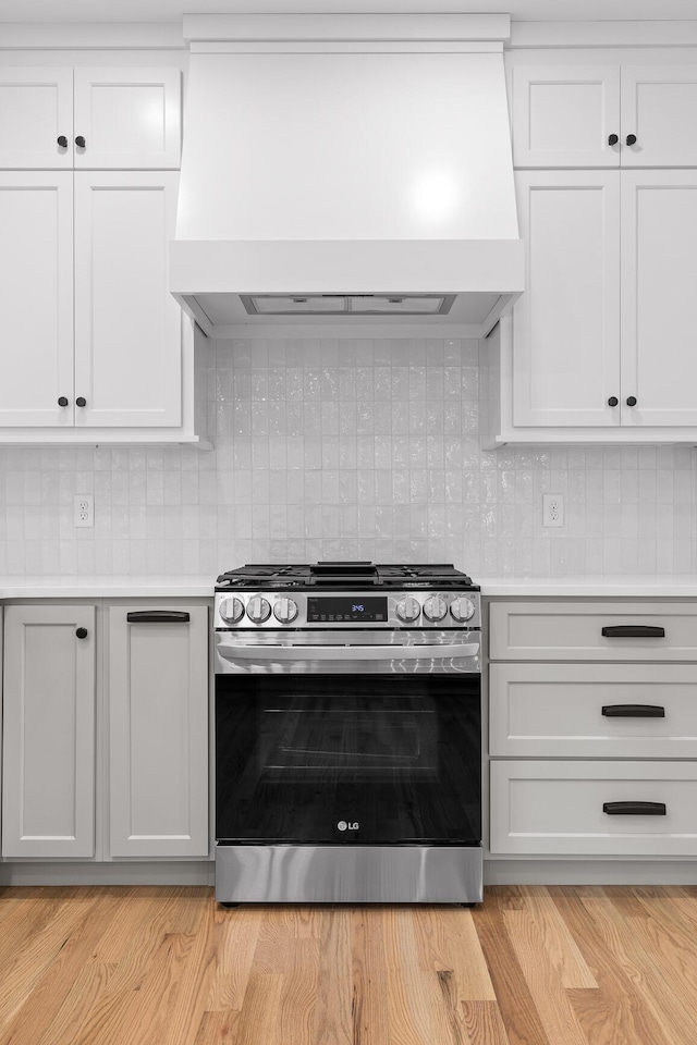 kitchen featuring light hardwood / wood-style flooring, white cabinetry, backsplash, custom range hood, and gas stove