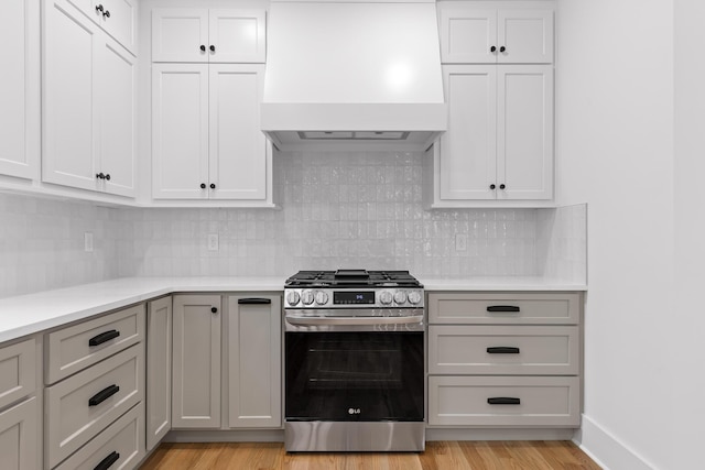 kitchen with backsplash, gas range, custom exhaust hood, and light hardwood / wood-style floors