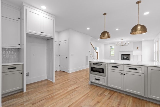 kitchen featuring gray cabinetry, hanging light fixtures, light wood-type flooring, stainless steel microwave, and backsplash