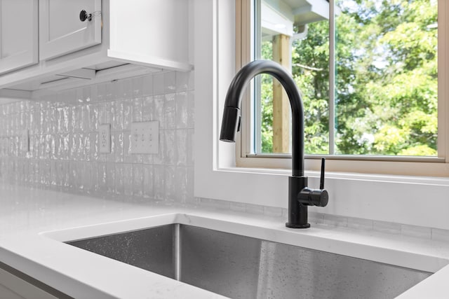 interior details featuring tasteful backsplash, white cabinetry, light stone countertops, and sink