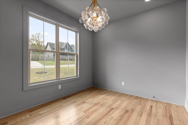 empty room featuring a notable chandelier, a healthy amount of sunlight, and light wood-type flooring