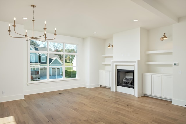 unfurnished living room featuring a chandelier, built in features, and light wood-type flooring