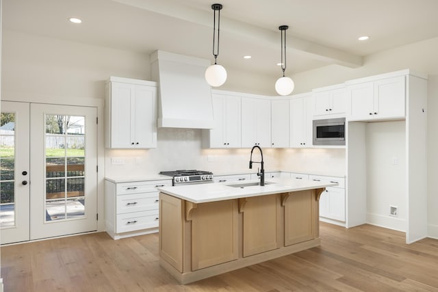 kitchen with white cabinetry, hanging light fixtures, sink, and a center island with sink