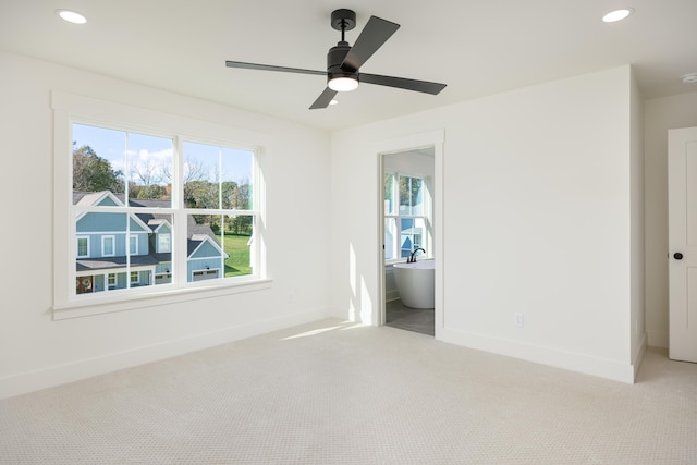 unfurnished bedroom with multiple windows, light carpet, connected bathroom, and ceiling fan