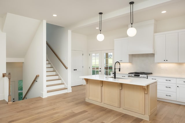 kitchen with french doors, sink, an island with sink, pendant lighting, and white cabinets