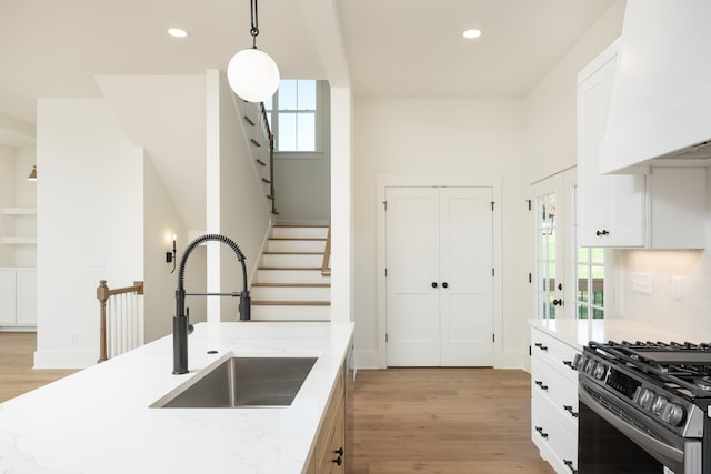 kitchen with light stone countertops, custom exhaust hood, sink, and hanging light fixtures