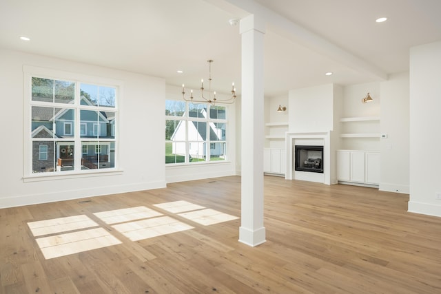 unfurnished living room with an inviting chandelier, built in features, and light hardwood / wood-style flooring