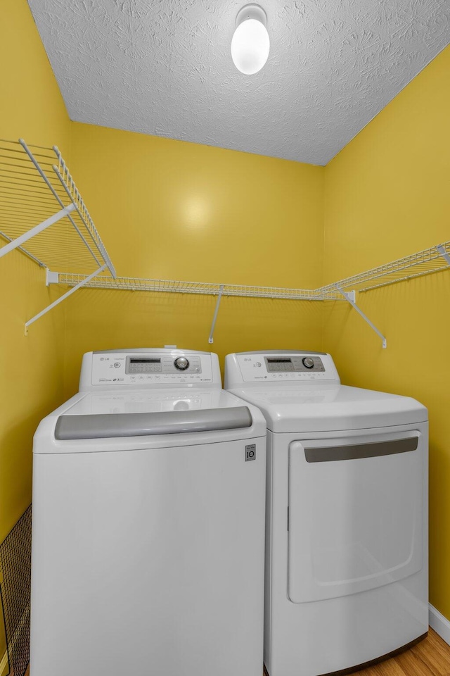 washroom featuring light wood-type flooring, a textured ceiling, and separate washer and dryer