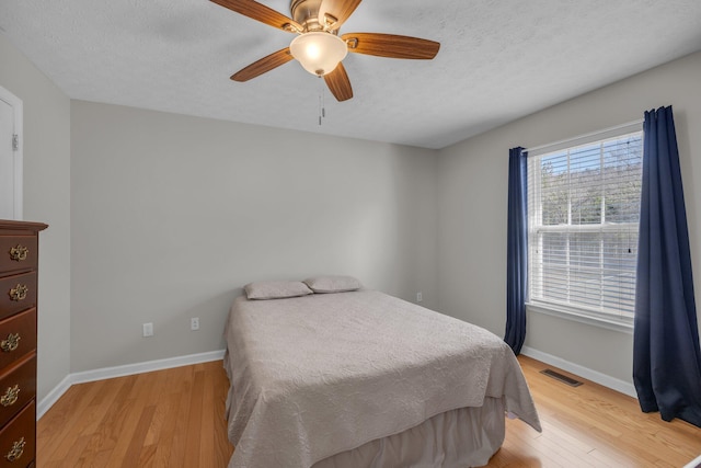 bedroom featuring ceiling fan, light hardwood / wood-style floors, and a textured ceiling