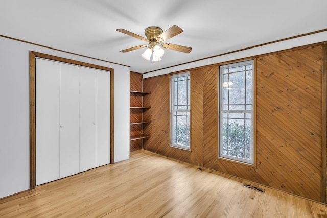 unfurnished bedroom with ceiling fan, wooden walls, ornamental molding, a closet, and light wood-type flooring