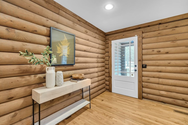 foyer entrance with log walls and light hardwood / wood-style floors