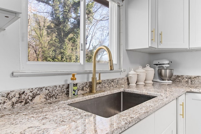 room details featuring white cabinetry, light stone countertops, and sink