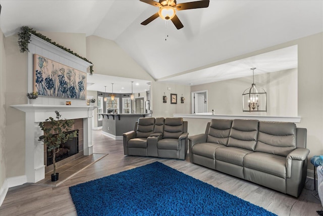 living room featuring ceiling fan with notable chandelier, wood-type flooring, lofted ceiling, and a fireplace