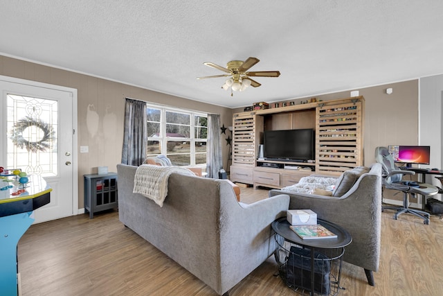 living room with wooden walls, ceiling fan, light hardwood / wood-style floors, crown molding, and a textured ceiling